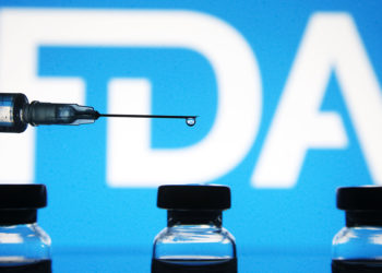 UKRAINE - 2021/01/01: In this photo illustration a medical syringe and vials are seen in front of the Food and Drug Administration (FDA) logo. 
The World Health Organization (WHO) on 31 December 2020 lists Pfizer/BioNTech vaccine for emergency use, as media reported. (Photo Illustration by Pavlo Gonchar/SOPA Images/LightRocket via Getty Images)