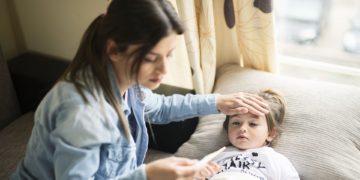 Mother checking temperature on sick daughter laying in bed